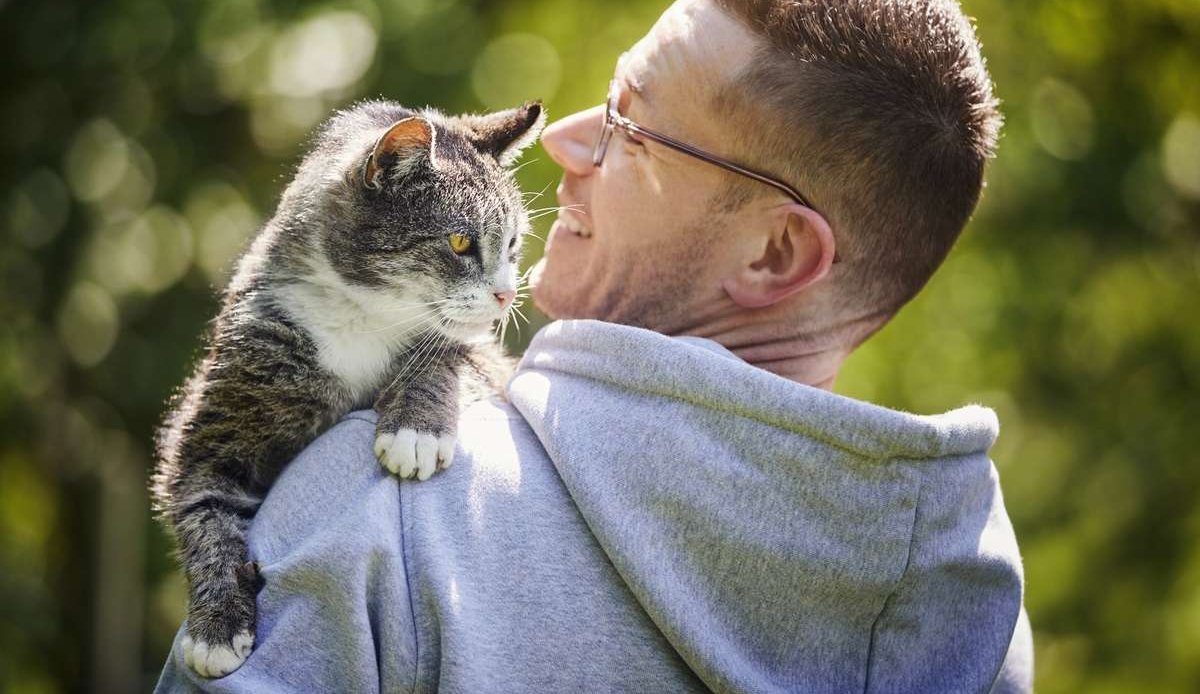 Un homme souriant portant son chat tigré âgé dans le jardin